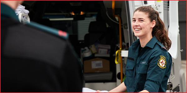 A smiling female paramedic at standing at the back of an ambulance